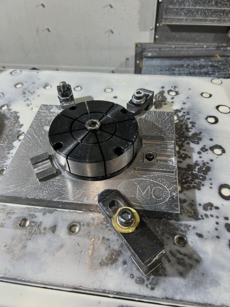 A round workholding fixture clamped to a subplate on a machining center table.